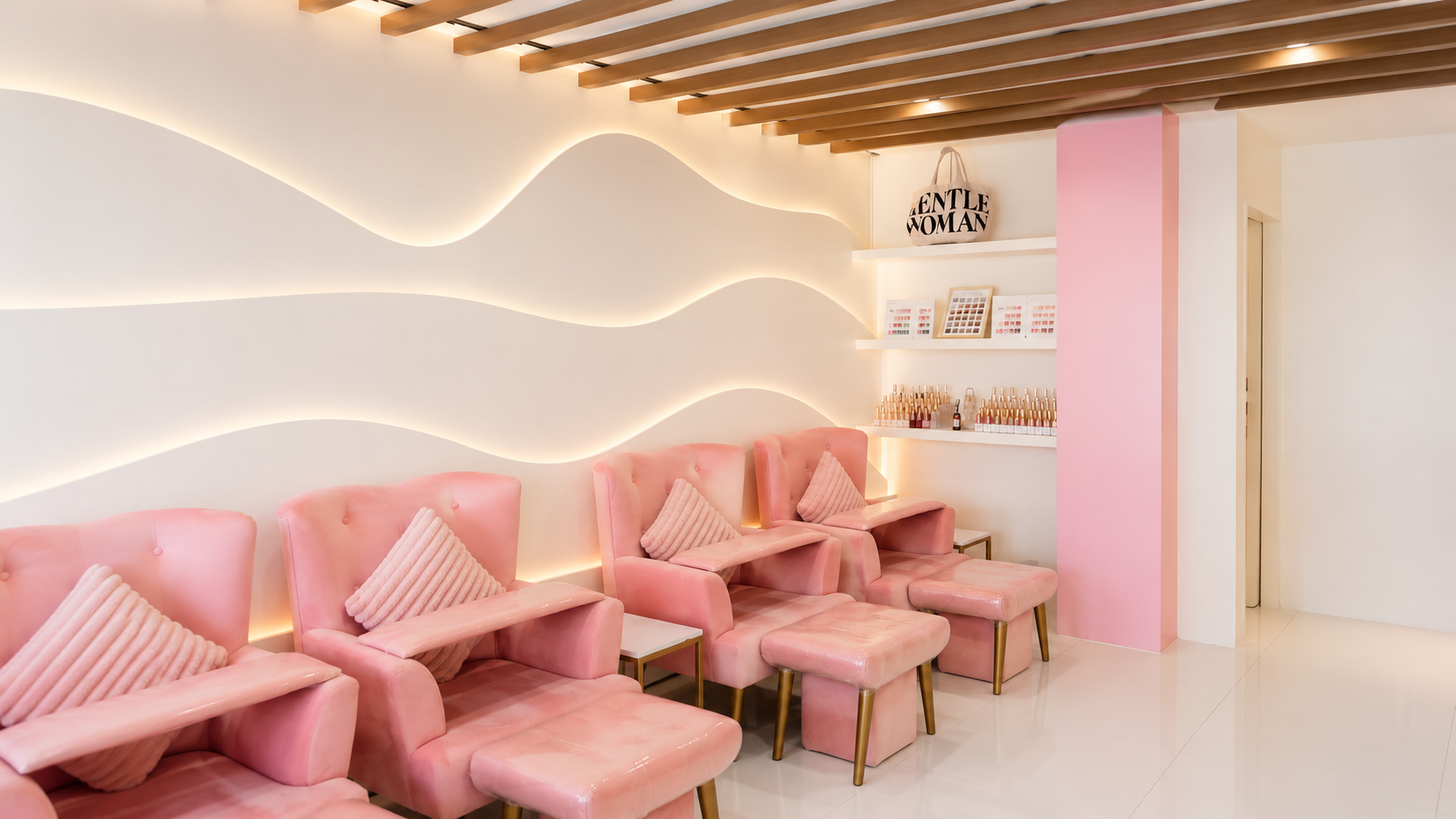 Pink pedicure lounge with blush chairs and a softly illuminated curved feature wall.
